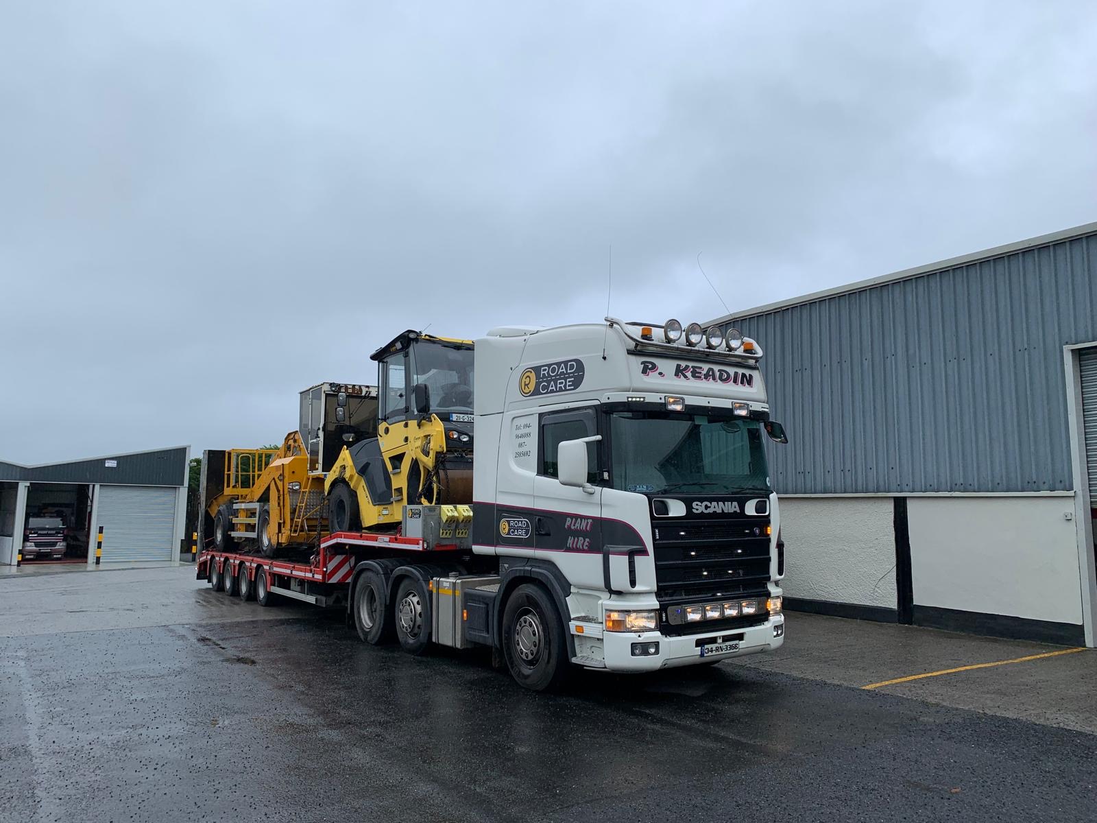 White Scania transporting yellow machinery